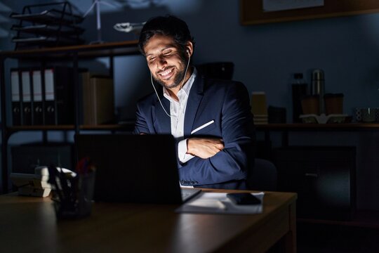 Handsome latin man working at the office at night happy face smiling with crossed arms looking at the camera. positive person.