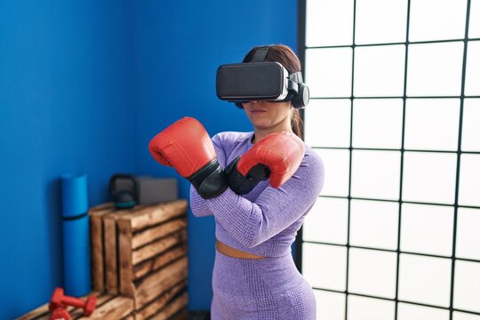 Young beautiful hispanic woman using virtual reality glasses boxing at sport center