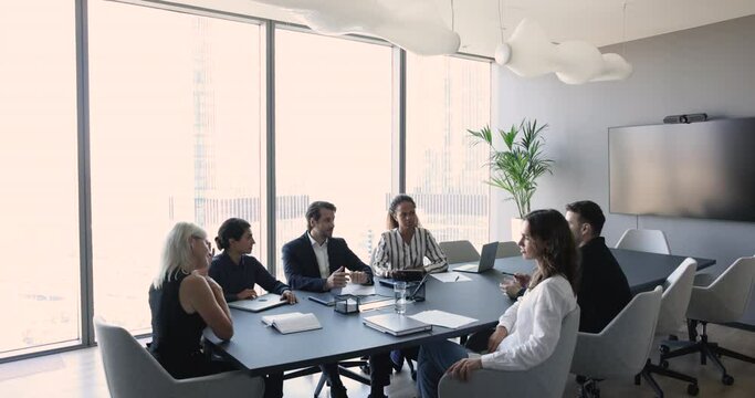Negotiations process of multi ethnic staff, businesspeople gathered in skyscraper office. Millennial team member, share strategy, discuss commercial deal with partners in boardroom. Business meeting