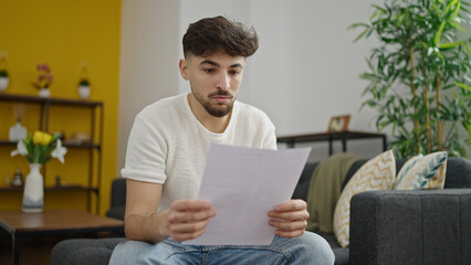 Young arab man reading paper sitting on sofa at home