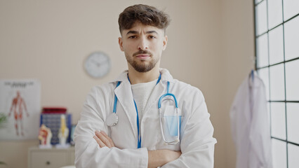 Young arab man doctor standing with arms crossed gesture and relaxed expression at clinic
