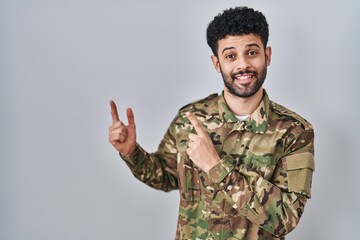 Arab man wearing camouflage army uniform smiling and looking at the camera pointing with two hands...