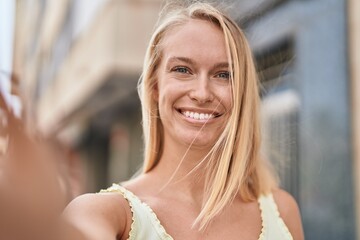 Young blonde woman smiling confident making selfie by the camera at street