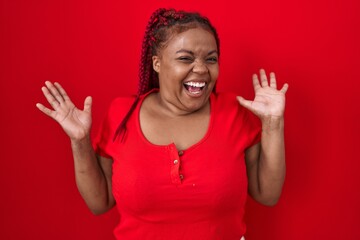 African american woman with braided hair standing over red background celebrating crazy and amazed for success with arms raised and open eyes screaming excited. winner concept