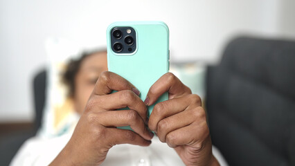 African american woman using smartphone lying on sofa at home