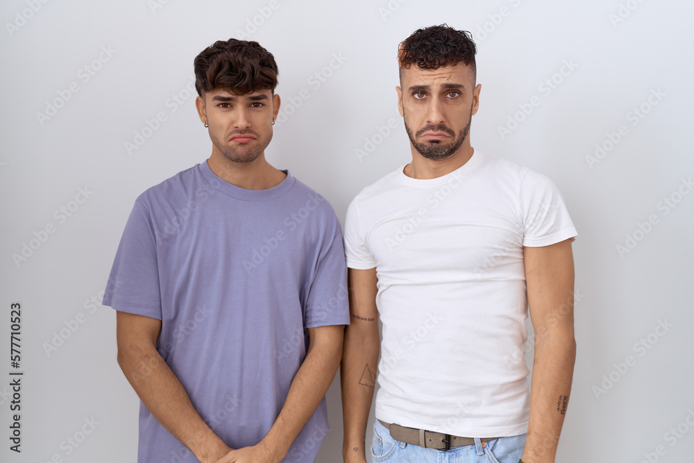 Poster homosexual gay couple standing over white background depressed and worry for distress, crying angry 