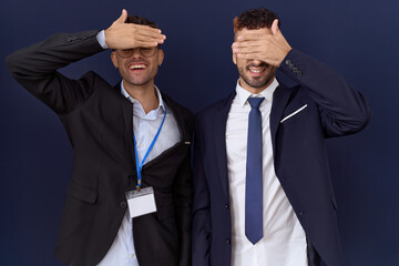 Two hispanic business men wearing business clothes smiling and laughing with hand on face covering...