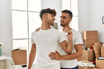 Two hispanic men couple hugging each other holding key of new house at new home