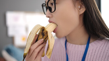 Young chinese woman preschool teacher eating banana at kindergarten