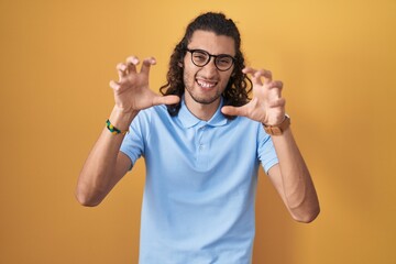 Fototapeta premium Young hispanic man standing over yellow background smiling funny doing claw gesture as cat, aggressive and sexy expression