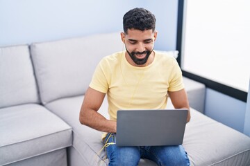 Young arab man using laptop sitting on sofa at home