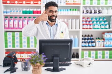 Hispanic man with beard working at pharmacy drugstore smiling doing phone gesture with hand and fingers like talking on the telephone. communicating concepts.