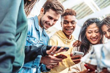 Fototapeta premium Diverse group of young people using smart mobile phone device outside - University students watching cellphone in college campus - Happy teenagers addicted to social media - Technology concept