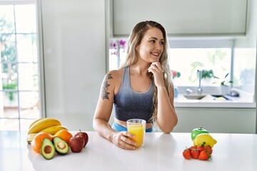 Young woman smiling confident holding orange juice at kitchen