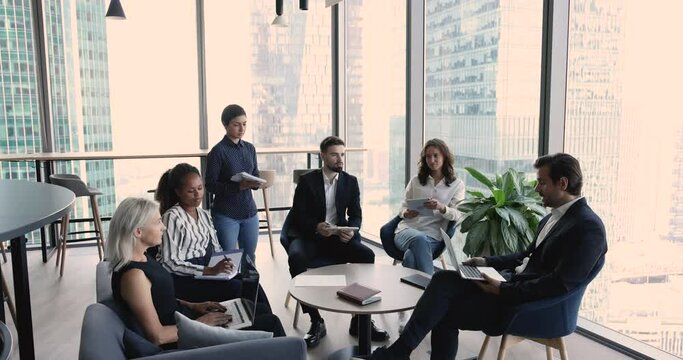 Group of multi ethnic employees listen company chief during morning briefing in skyscraper building. Team leader share opinion, corporate goal, talk about collaborative project to diverse office staff