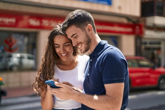 Young hispanic couple smiling confident using smartphone at street