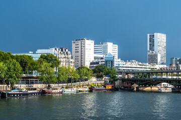 River Seine In Paris, France With Promenade, Anchored Houseboats And Modern Office Buildings
