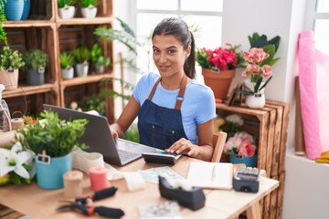 Young beautiful hispanic woman florist using laptop and calculator at florist