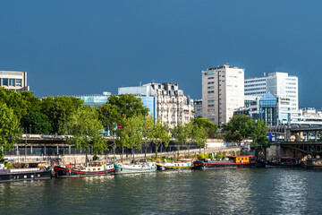 River Seine In Paris, France With Promenade, Anchored Houseboats And Modern Office Buildings