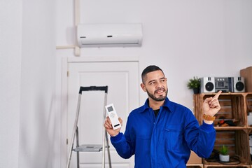 Hispanic repairman working with air conditioner smiling happy pointing with hand and finger to the side