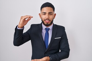 Young hispanic man wearing business suit and tie gesturing with hands showing big and large size sign, measure symbol. smiling looking at the camera. measuring concept.