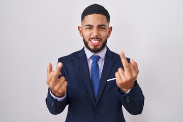 Young hispanic man wearing business suit and tie showing middle finger doing fuck you bad expression, provocation and rude attitude. screaming excited