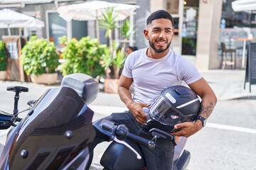 Fototapeta na wymiar Young latin man holding helmet sitting on motorbike at street