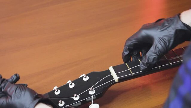 man with guitar,master hands in gloves puts on new strings and tuning with pegs on classical guitar,wooden red,pulls strings on fretboard twisting pegs,workshop.concept repair of musical instruments.