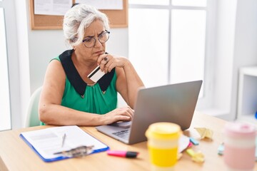 Middle age grey-haired woman business worker using laptop and credit card at office