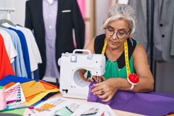 Middle age grey-haired woman tailor using sewing machine with serious expression at tailor shop