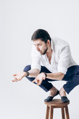Portrait of a handsome man with a beard in a white shirt sits on a chair
