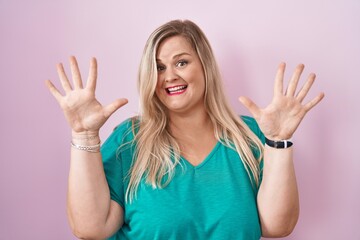 Caucasian plus size woman standing over pink background showing and pointing up with fingers number ten while smiling confident and happy.