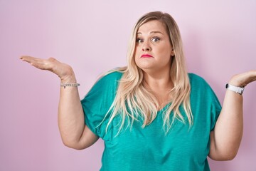 Caucasian plus size woman standing over pink background clueless and confused expression with arms and hands raised. doubt concept.