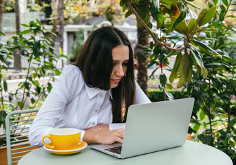 Young woman works with laptop on terrace of  cafe. Hunched posture, professional spinal deformity concept. - obrazy, fototapety, plakaty
