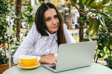 Young woman works with laptop on terrace of  cafe. Hunched posture, professional spinal deformity...
