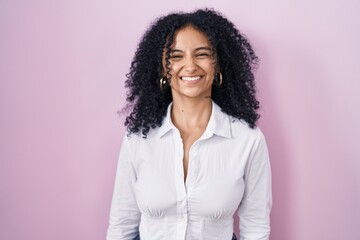 Hispanic woman with curly hair standing over pink background with a happy and cool smile on face....