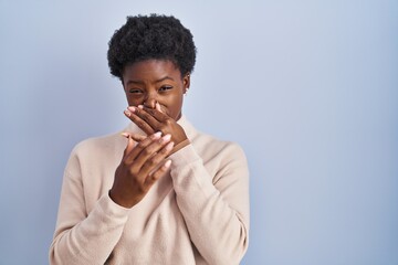 African american woman standing over blue background smelling something stinky and disgusting,...