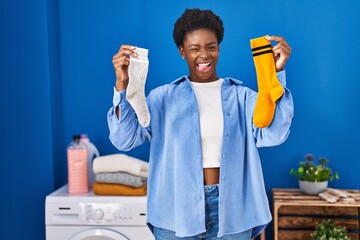 African american woman holding clean andy dirty socks sticking tongue out happy with funny...