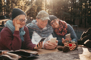 Fototapeta na wymiar Group of friends or family sitting in outdoors at wooden table in the woods while checking their mobile phones