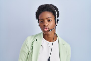 African american woman wearing call center agent headset looking at the camera blowing a kiss on...