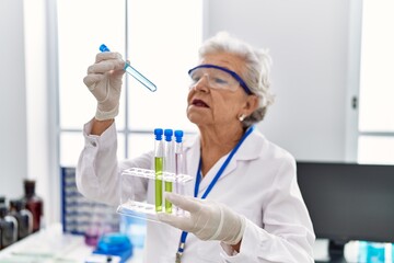 Fototapeta premium Senior grey-haired woman wearing scientist uniform holding test tubes at laboratory