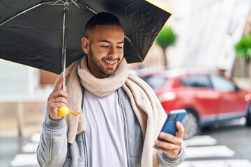 African american man using smartphone holding umbrella at street
