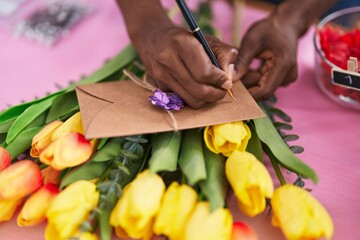 African american woman florist smiling confident writing on envelope letter at flower shop