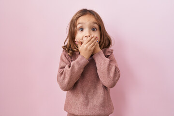 Little hispanic girl standing over pink background shocked covering mouth with hands for mistake....