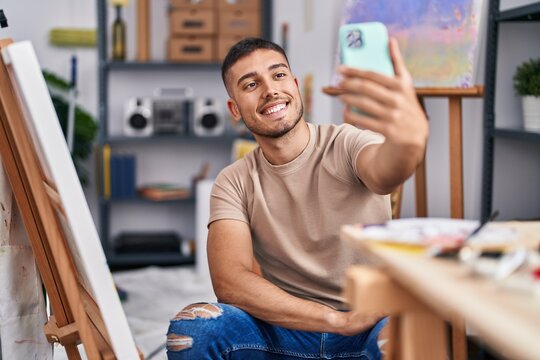 Young hispanic man artist making selfie by the smartphone at art studio