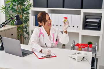 Middle age woman wearing doctor uniform holding urine analysis test tube at clinic