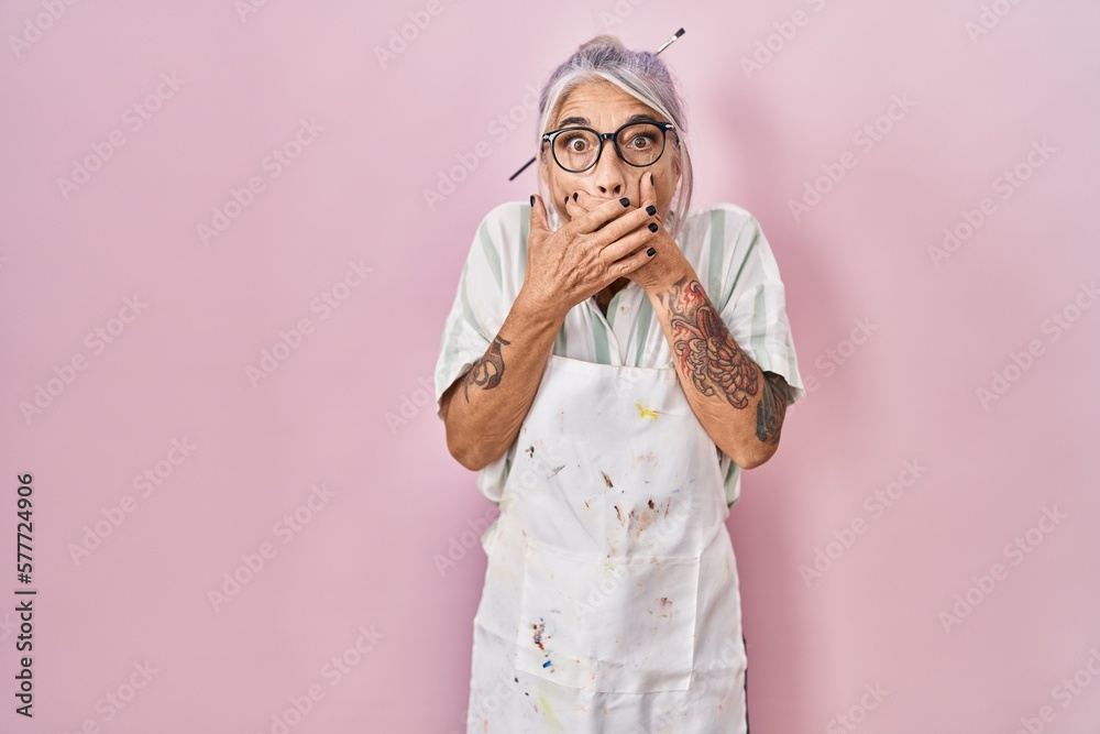 Sticker middle age woman with grey hair wearing artist look shocked covering mouth with hands for mistake. s