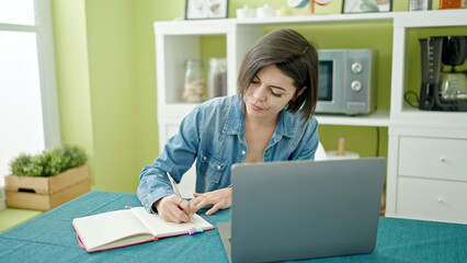 Young caucasian woman using laptop writing on notebook at home