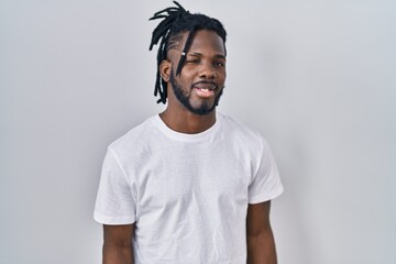 African man with dreadlocks wearing casual t shirt over white background winking looking at the...