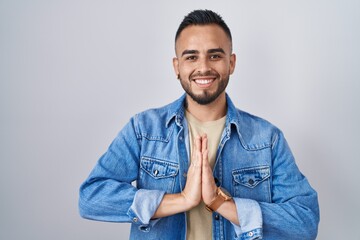Young hispanic man standing over isolated background praying with hands together asking for...